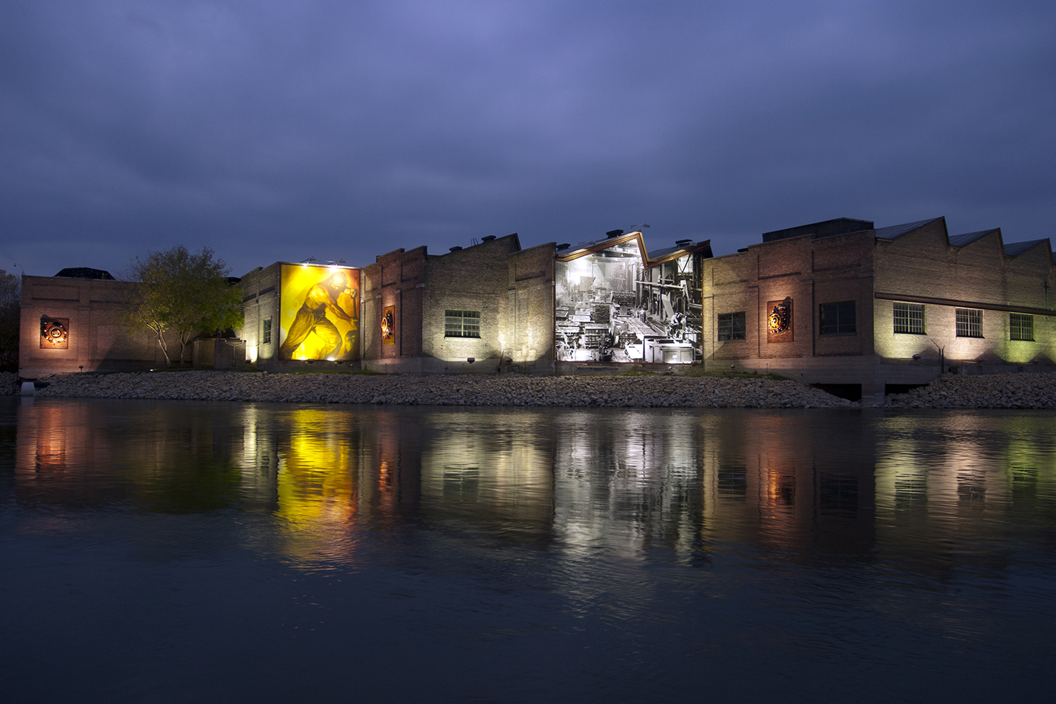 Buildings with murals are lit up at night with their mirror images shimmering in the water.