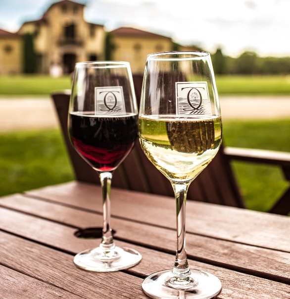 Two glasses of wine — one red, one white — sit atop a wooden table outside of a vineyard in Beloit, WI.